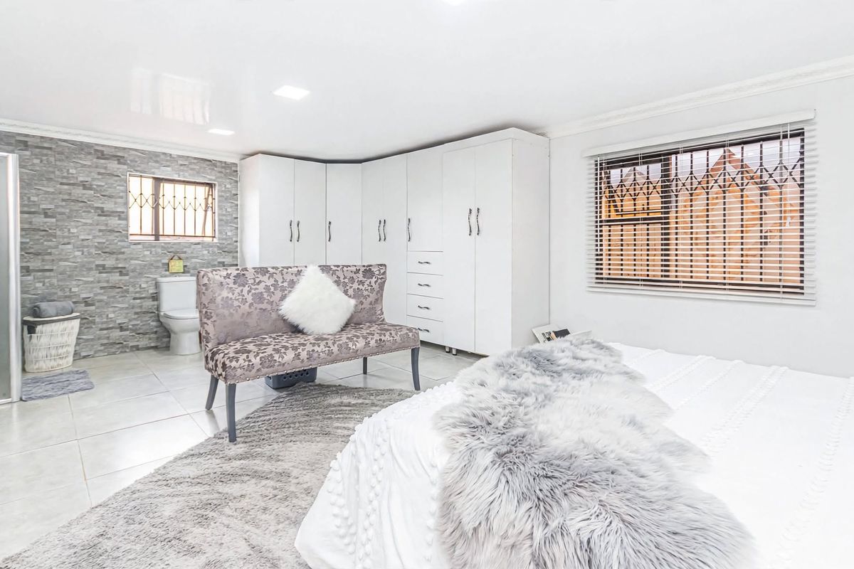 Spacious bedroom featuring built-in cupboards, tiled flooring, and an integrated en-suite bathroom with modern finishes and security features.