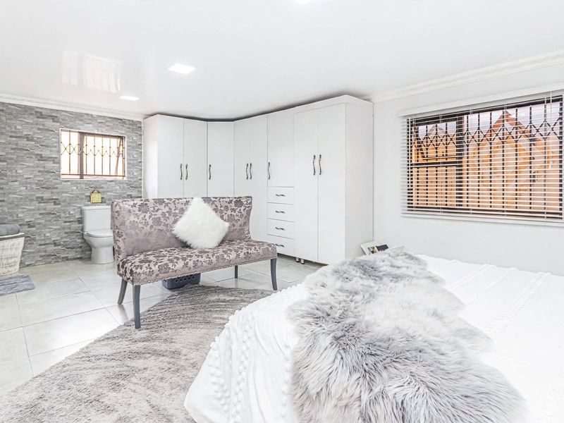 Spacious bedroom featuring built-in cupboards, tiled flooring, and an integrated en-suite bathroom with modern finishes and security features.