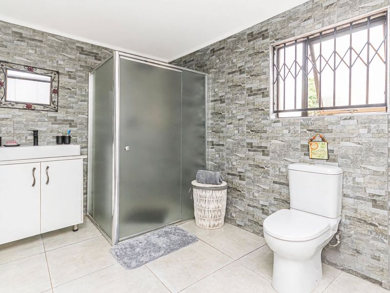 Modern bathroom featuring a glass shower enclosure, vanity cabinet with basin, and toilet, finished with textured stone-look wall tiles and neutral floor tiles.