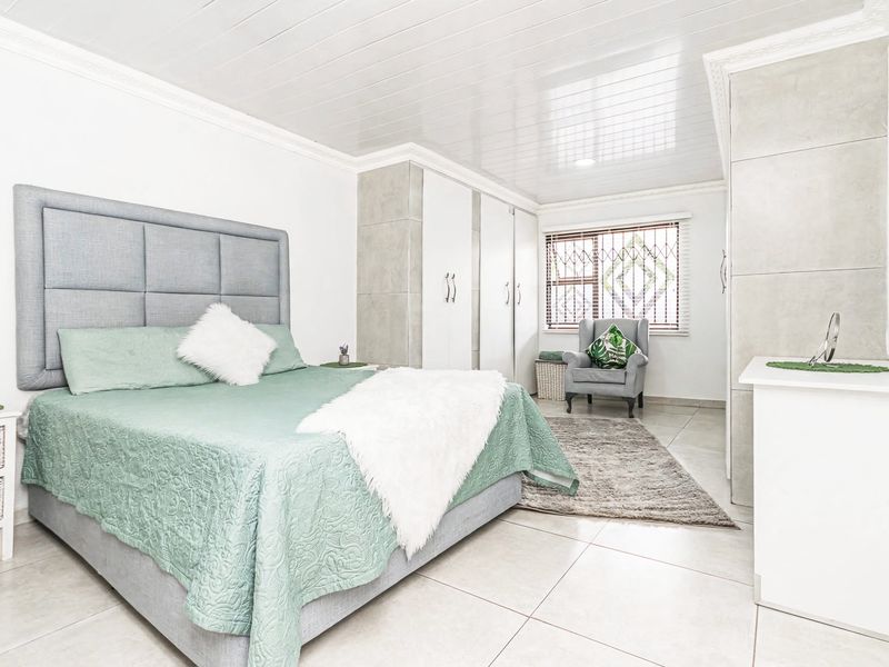 A well-maintained bedroom featuring built-in cupboards, tiled flooring, and a glossy ceiling finish with decorative cornicing.