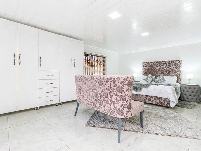 Spacious bedroom featuring large built-in cupboards, tiled flooring, and recessed ceiling lighting, offering a clean and well-maintained living space.