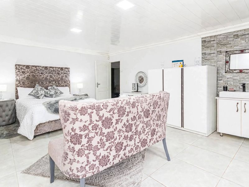 Spacious bedroom featuring tiled flooring, a stone-cladding accent wall with a built-in vanity, and recessed ceiling lighting.
