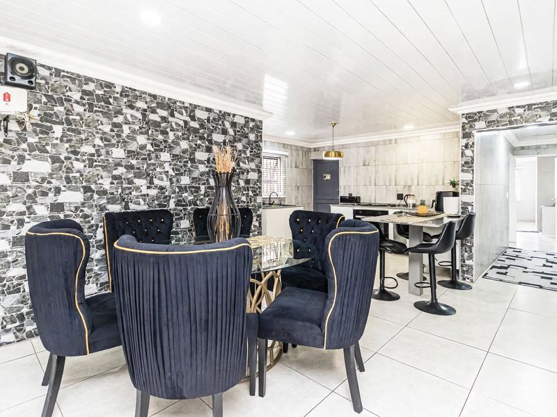 Open-plan living and dining area featuring a modern kitchen with breakfast bar, tiled flooring, and a distinctive stone-cladding feature wall.
