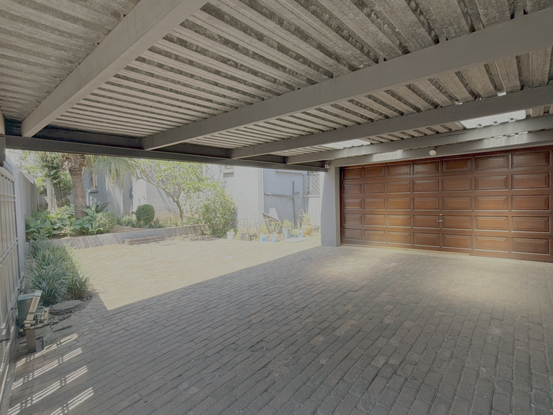 A spacious covered carport area featuring a sectional garage door, brick paving, and a sturdy metal roof structure.