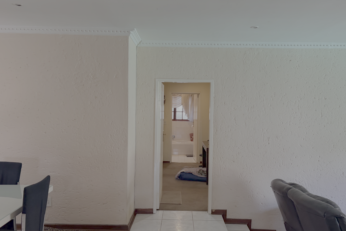 A living area featuring textured walls, decorative cornicing, and recessed lighting, with a doorway leading through to a bathroom area.
