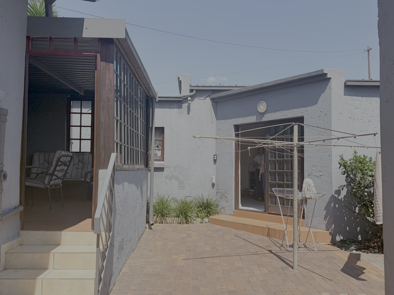 Rear courtyard area featuring paved flooring, a covered patio section, and direct access to the main dwelling via tiled steps.