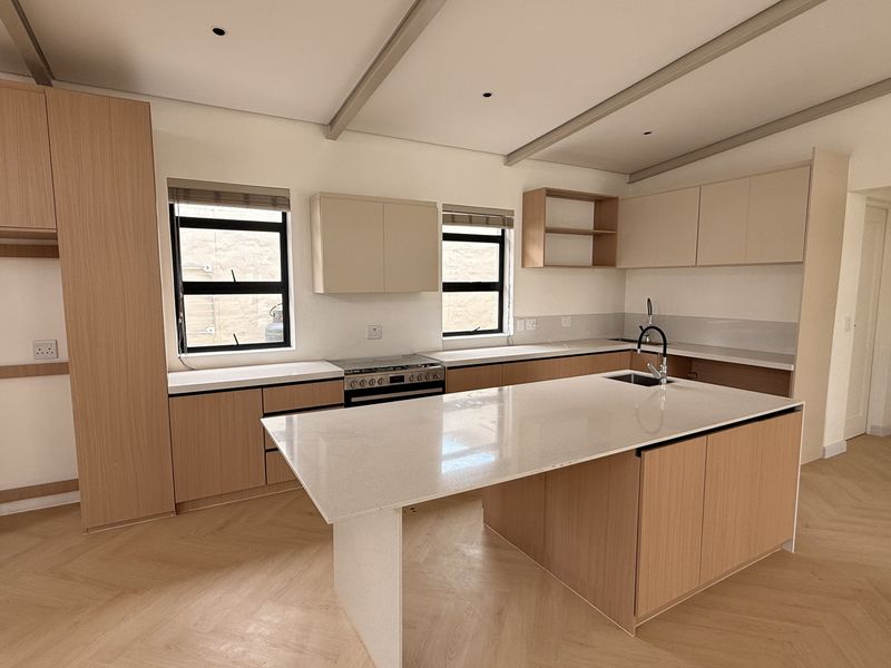 Modern, spacious kitchen featuring light wood cabinetry, a large central island with quartz countertops, and elegant herringbone flooring in a clean, empty space.