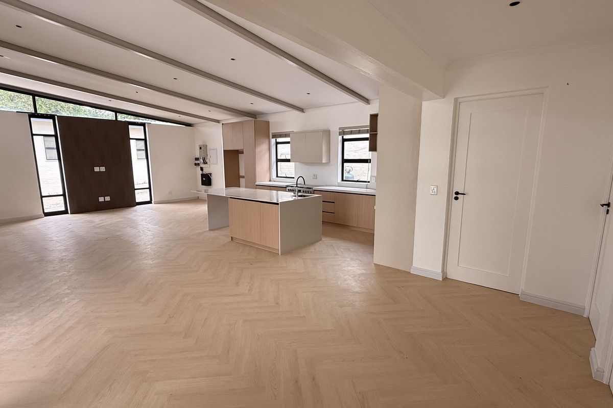 Spacious open-plan living and kitchen area featuring modern light wood cabinetry, a central island, and elegant herringbone timber flooring throughout.
