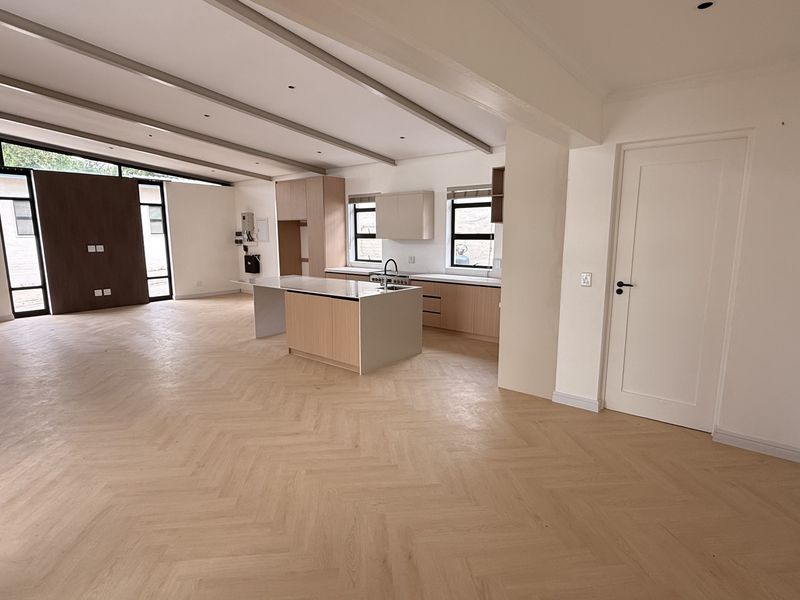 Spacious open-plan living and kitchen area featuring modern light wood cabinetry, a central island, and elegant herringbone timber flooring throughout.