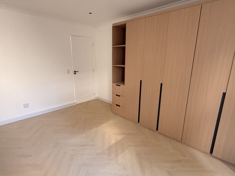 A bright, empty bedroom featuring modern light wood herringbone flooring and extensive floor-to-ceiling built-in cabinetry with integrated shelving.