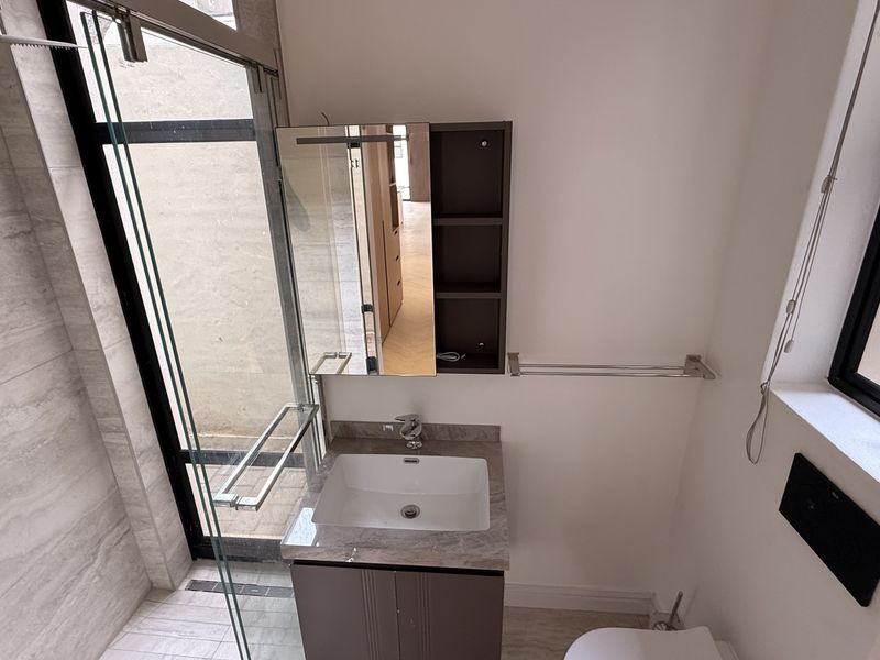 Modern bathroom featuring a vanity with stone countertop, glass-enclosed shower with rain head, and contemporary fixtures in a clean, well-maintained space.