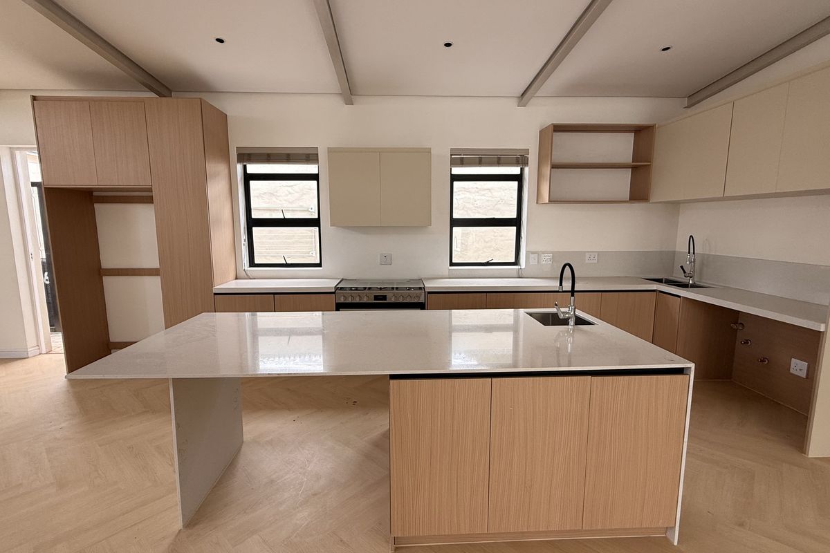 Modern, newly renovated kitchen featuring a large central island, quartz countertops, light wood cabinetry, and elegant herringbone flooring in an open-plan layout.