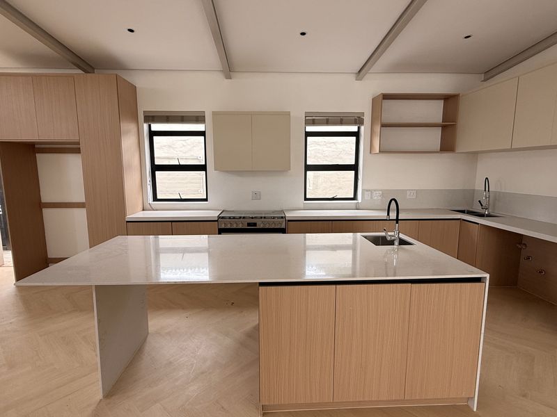 Modern, newly renovated kitchen featuring a large central island, quartz countertops, light wood cabinetry, and elegant herringbone flooring in an open-plan layout.