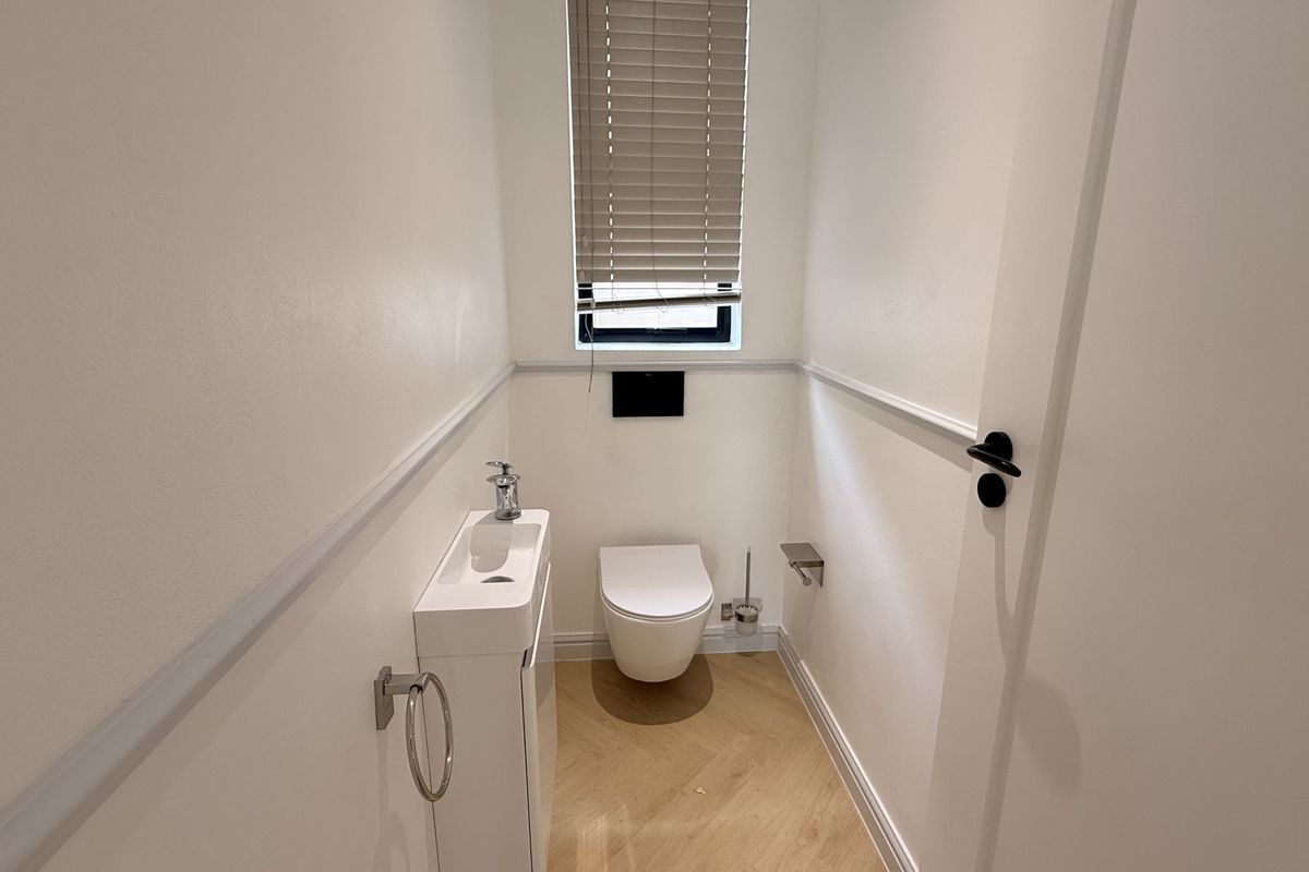 A modern, compact guest powder room featuring a wall-mounted toilet, sleek vanity basin, wainscoting detail, and light timber-look flooring.