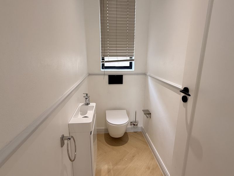 A modern, compact guest powder room featuring a wall-mounted toilet, sleek vanity basin, wainscoting detail, and light timber-look flooring.