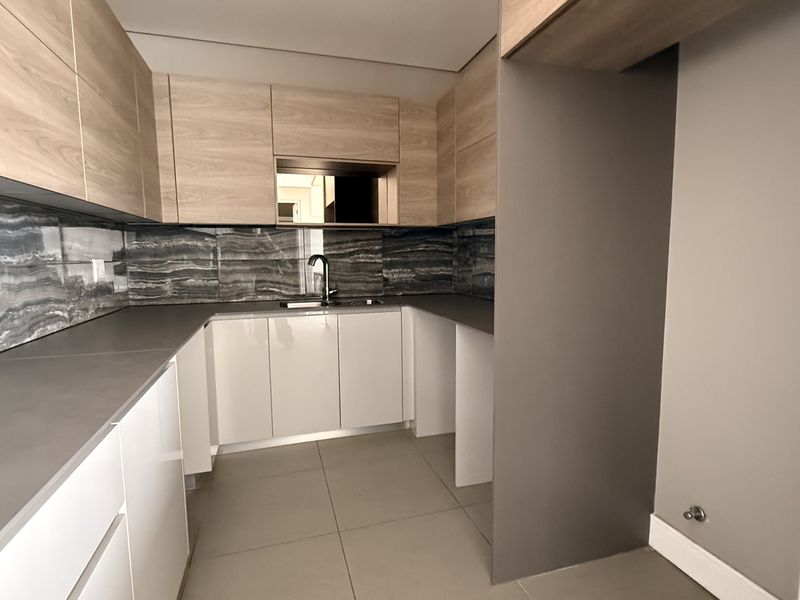Modern kitchen featuring sleek wood-tone and white cabinetry, dark stone countertops, a stylish tiled backsplash, and high-quality fixtures in a clean, contemporary layout.