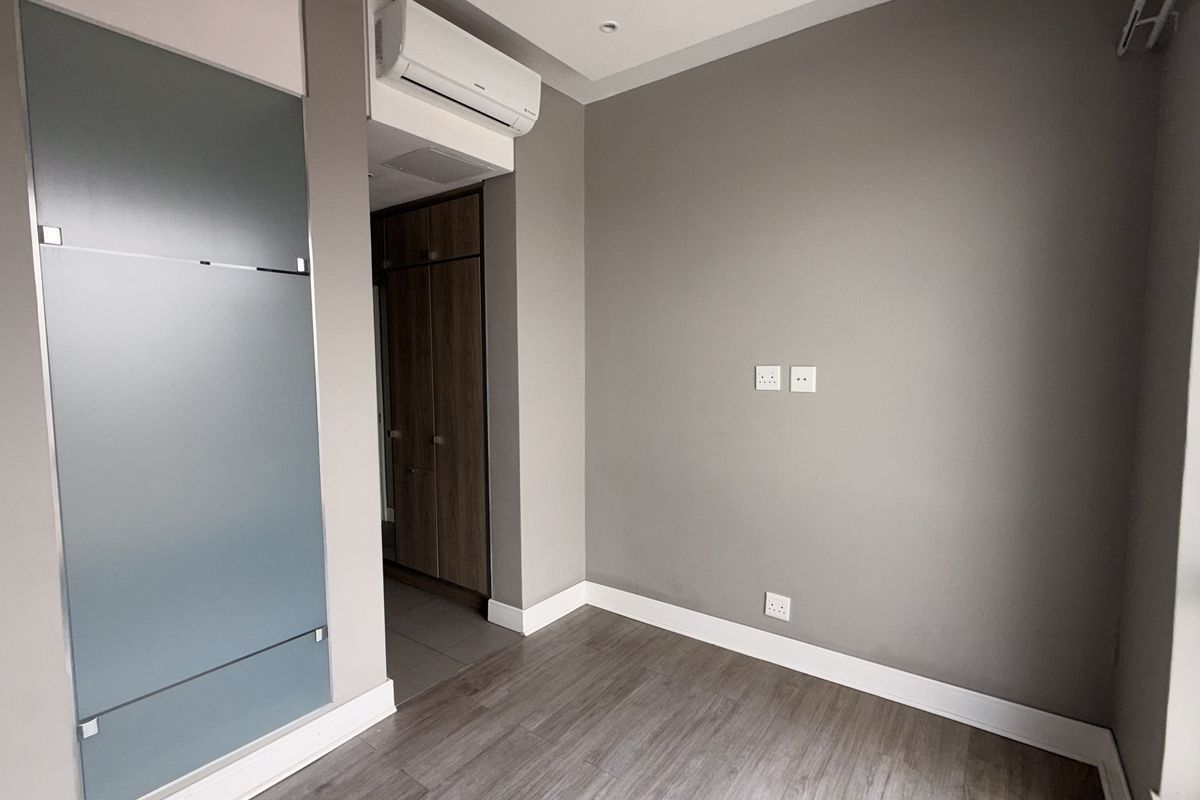 A modern, empty bedroom featuring laminate flooring, built-in cupboards, and a wall-mounted air conditioning unit, offering a clean and neutral living space.