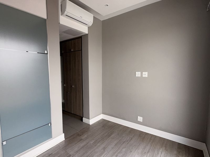 A modern, empty bedroom featuring laminate flooring, built-in cupboards, and a wall-mounted air conditioning unit, offering a clean and neutral living space.