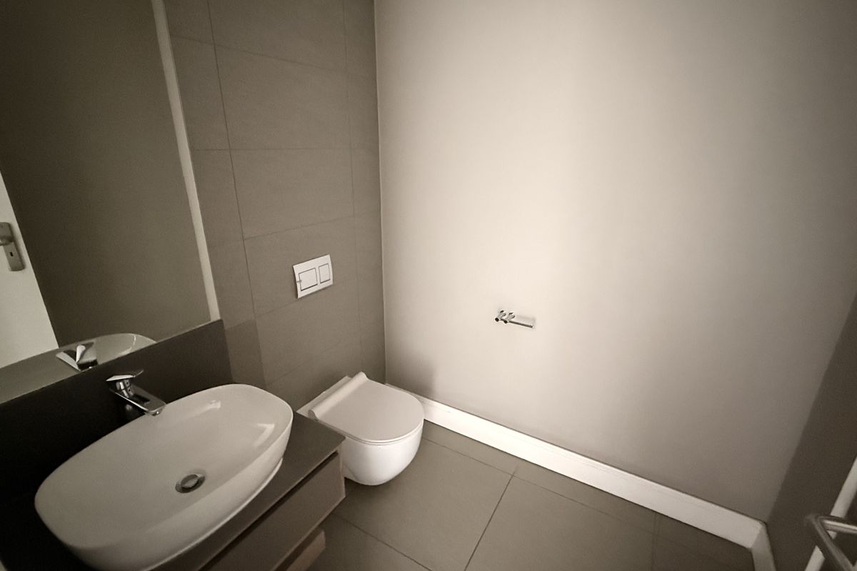 A modern, minimalist guest bathroom featuring a wall-mounted toilet, vanity basin with mixer tap, and neutral floor-to-ceiling tiling.