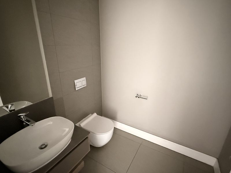 A modern, minimalist guest bathroom featuring a wall-mounted toilet, vanity basin with mixer tap, and neutral floor-to-ceiling tiling.