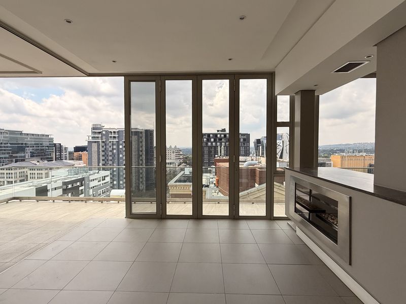 Spacious covered penthouse balcony featuring sleek tiled flooring, a modern built-in fireplace, and expansive bi-fold glass doors offering panoramic city views.