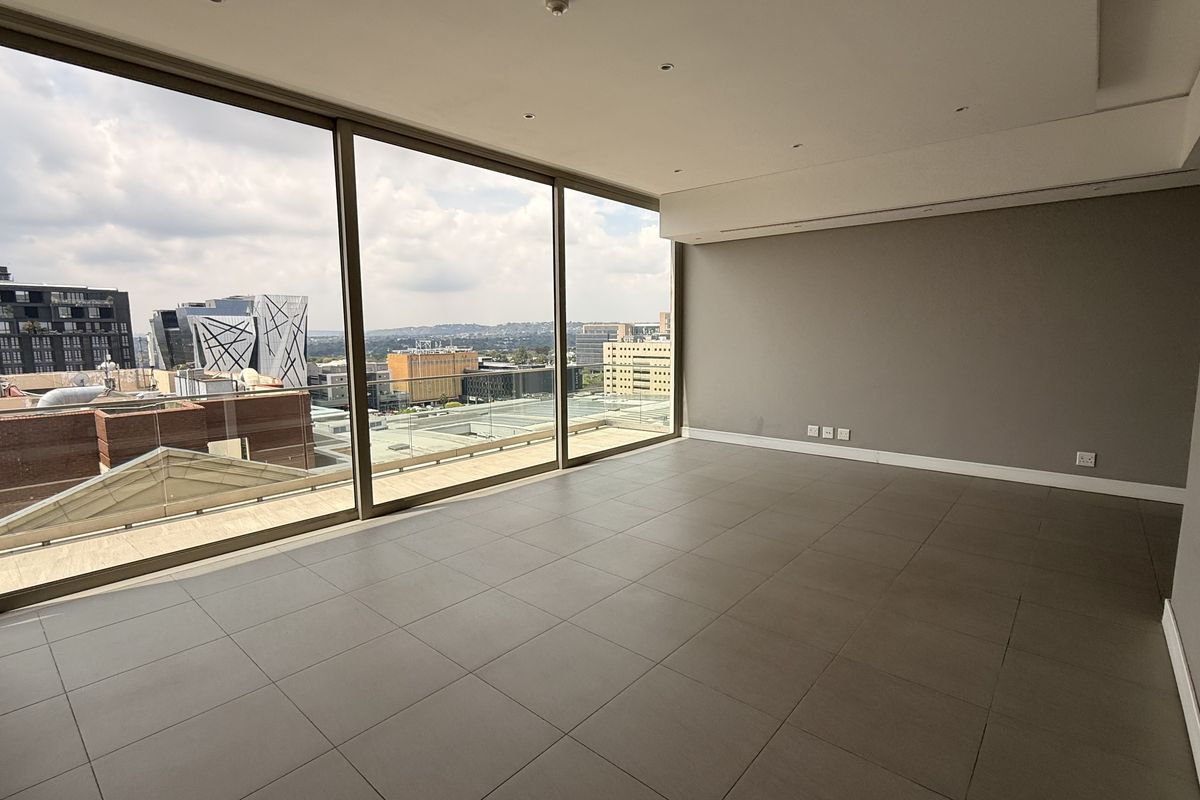 Spacious, empty living area featuring large floor-to-ceiling windows with expansive city views, neutral tiled flooring, and modern recessed ceiling lighting.