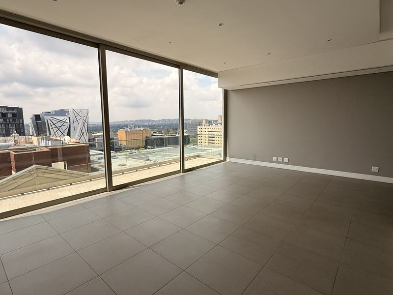 Spacious, empty living area featuring large floor-to-ceiling windows with expansive city views, neutral tiled flooring, and modern recessed ceiling lighting.