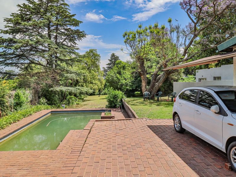 Outdoor area featuring a brick-paved patio, a swimming pool, and a spacious garden with mature trees.