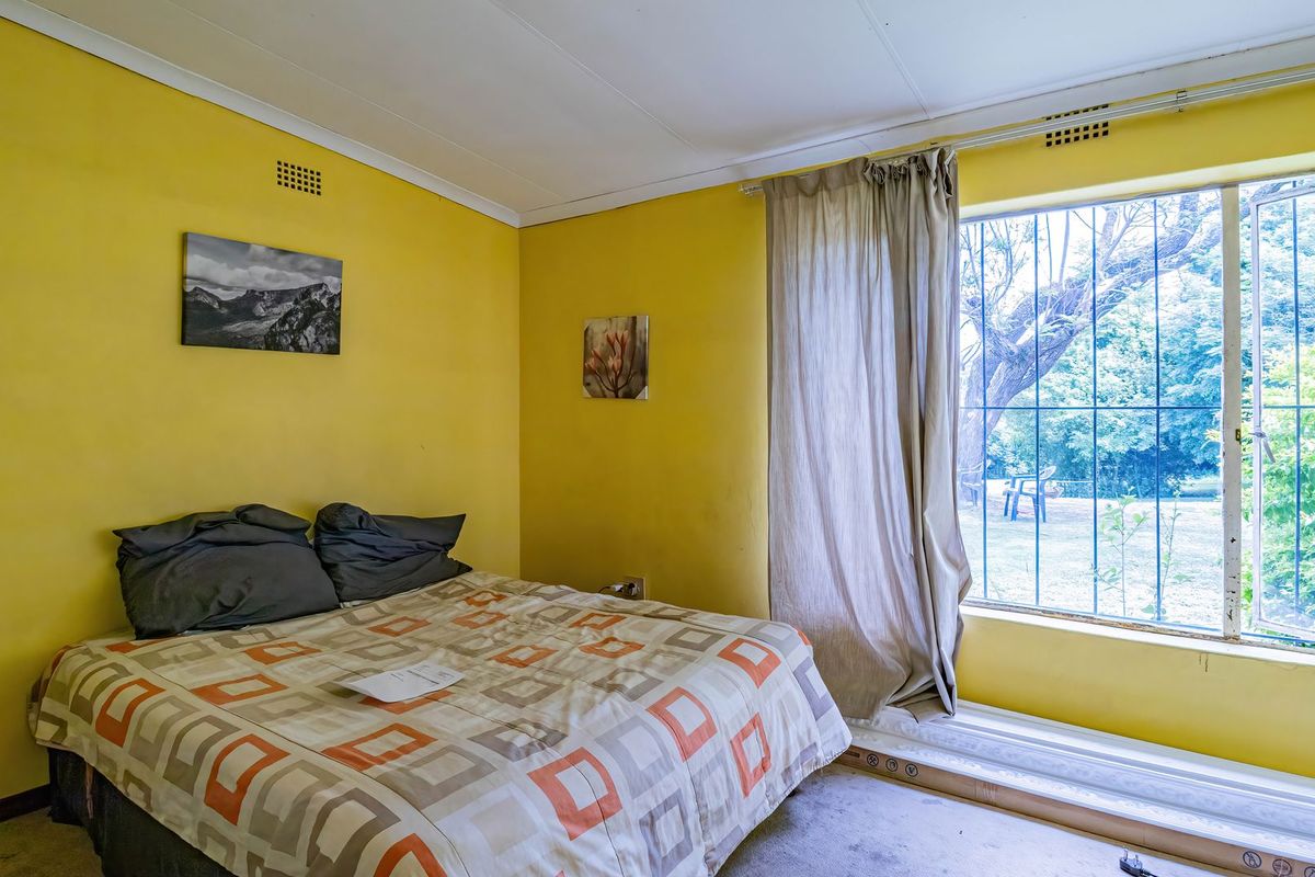 A bedroom featuring yellow walls, carpet flooring, and a large window with security bars overlooking the garden.