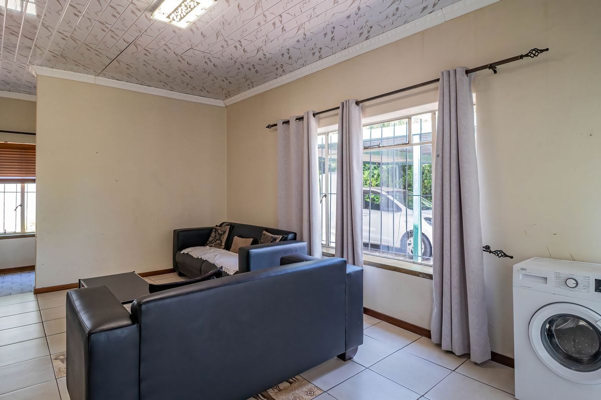 A living area featuring tiled flooring and decorative ceiling tiles, with security bars on the windows and neutral wall finishes.