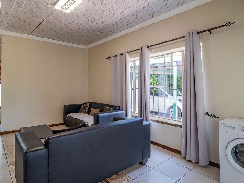 A living area featuring tiled flooring and decorative ceiling tiles, with security bars on the windows and neutral wall finishes.