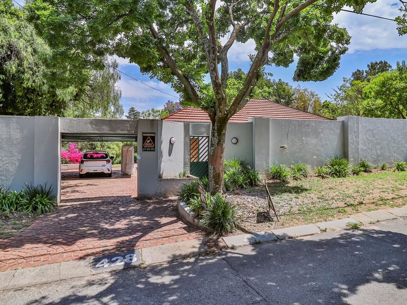 Front elevation of the property featuring a secure perimeter wall, paved driveway, and a covered carport area.