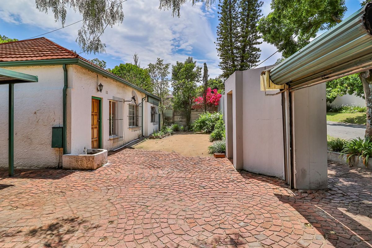 Rear exterior view of the property featuring a brick-paved courtyard, carport structure, and established garden area with security features.