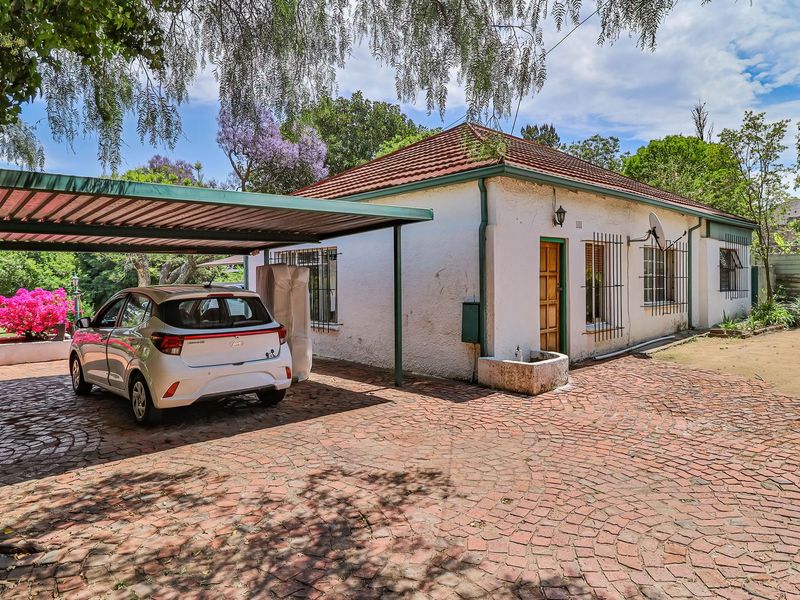 Front view of a single-story house featuring a tiled roof, a covered carport, and a paved driveway set within a landscaped garden.
