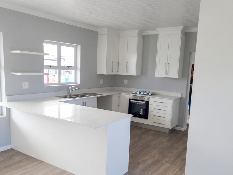 Modern, bright kitchen featuring white cabinetry, quartz countertops, built-in oven, and floating shelves, finished with light wood-look laminate flooring and a clean aesthetic.