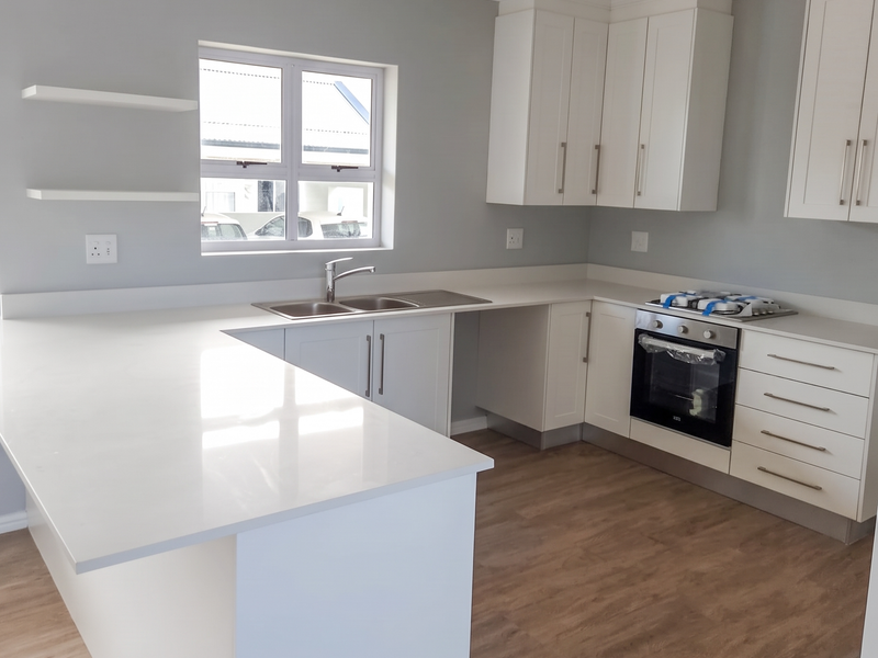 A modern, bright kitchen featuring white shaker cabinetry, quartz countertops, built-in oven, hob, and wood-look laminate flooring.