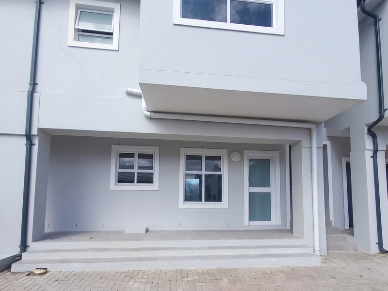 A modern rear exterior view of the apartment featuring a paved patio area, clean rendered facade, and well-maintained external fixtures.