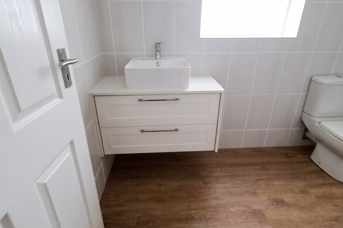 A clean, modern bathroom featuring a wall-mounted vanity with a vessel sink, wood-look flooring, and white tiled walls.