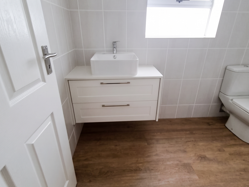 A clean, modern bathroom featuring a wall-mounted vanity with a vessel sink, wood-look flooring, and white tiled walls.