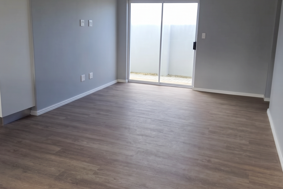 A bright, empty living room featuring modern laminate flooring, a panelled ceiling with recessed lighting, and a sliding glass door leading to the exterior.