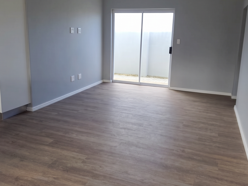 A bright, empty living room featuring modern laminate flooring, a panelled ceiling with recessed lighting, and a sliding glass door leading to the exterior.