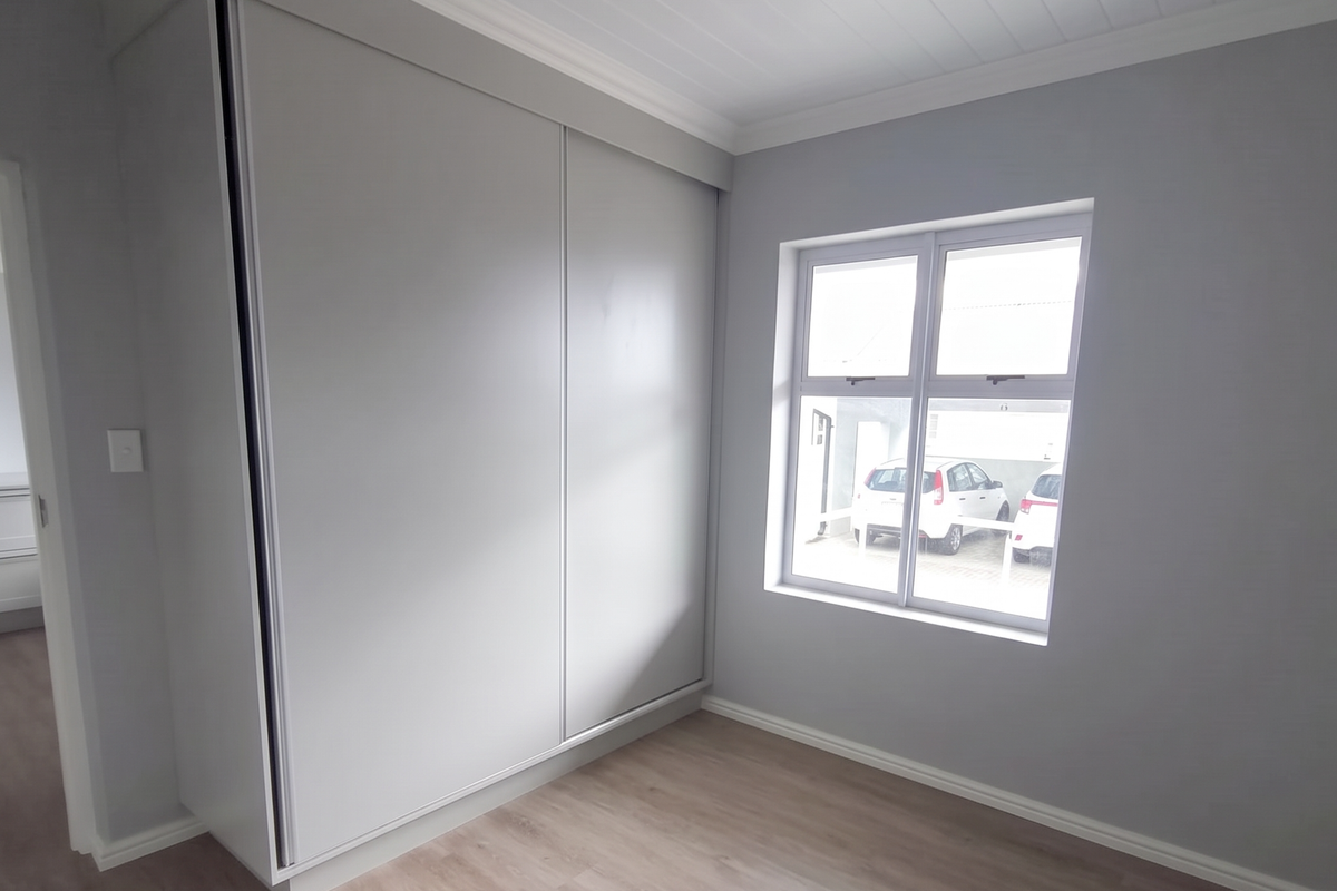 A bright, empty bedroom featuring modern laminate flooring, a built-in sliding door wardrobe, and a tongue and groove ceiling.