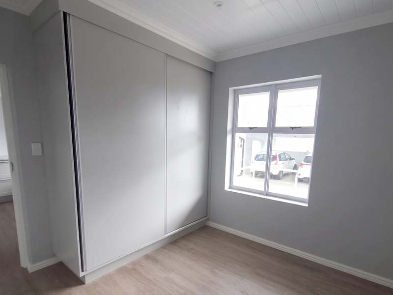 A bright, empty bedroom featuring modern laminate flooring, a built-in sliding door wardrobe, and a tongue and groove ceiling.
