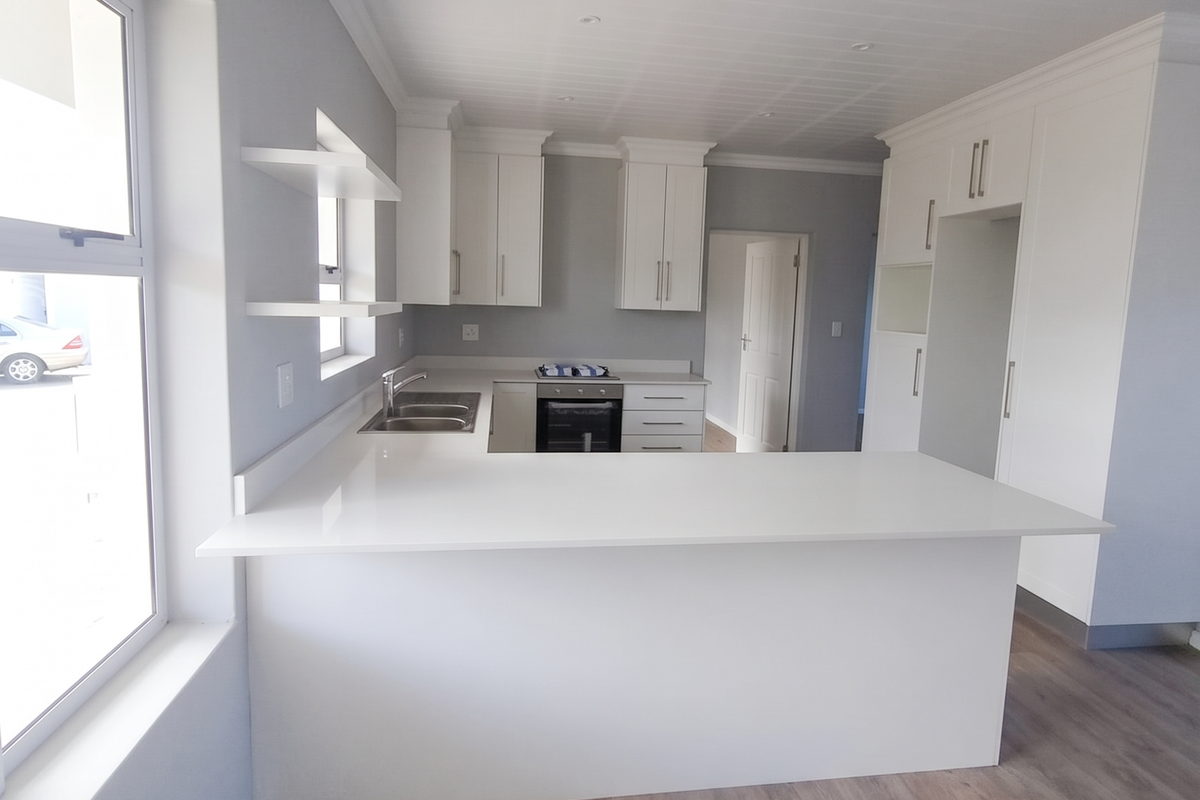 Modern, bright kitchen featuring white cabinetry, quartz countertops, integrated oven, and wood-look laminate flooring in an open-plan layout.