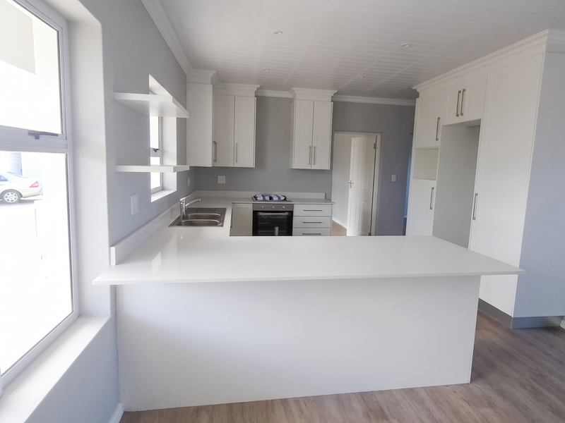 Modern, bright kitchen featuring white cabinetry, quartz countertops, integrated oven, and wood-look laminate flooring in an open-plan layout.