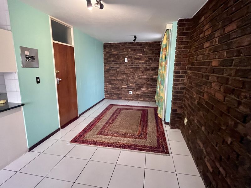 Open plan living area featuring exposed brick walls, ceramic floor tiles, and an adjacent kitchen area with built-in counter and sink.