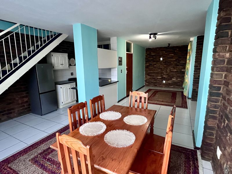 Open-plan living and dining area featuring exposed brick walls, tiled flooring, and an integrated kitchen space with a staircase leading to the upper level.