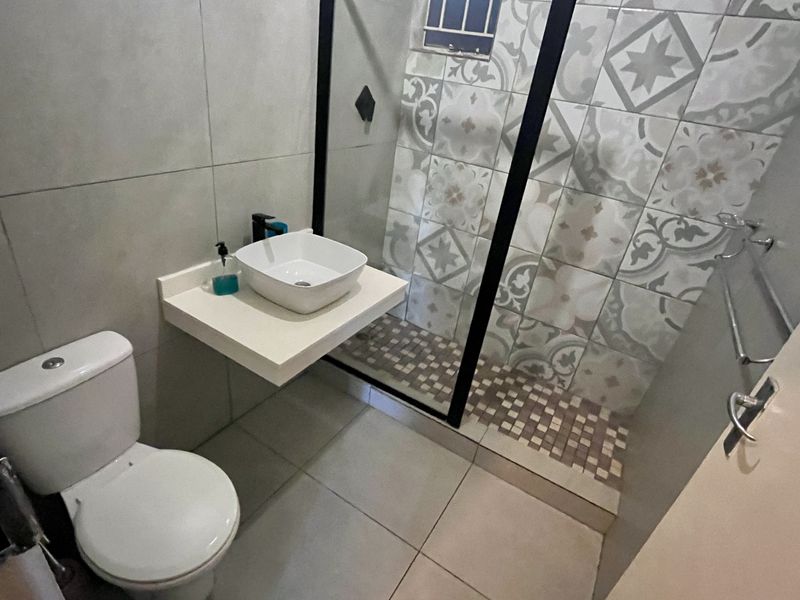 Modern bathroom featuring a floating vanity with a vessel sink, a walk-in shower with black-framed glass, and decorative patterned wall tiles.