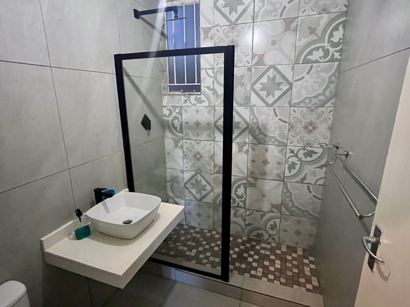 Modern bathroom featuring a walk-in shower with a black-framed glass screen, patterned feature wall tiles, and a contemporary floating vanity with a vessel sink.