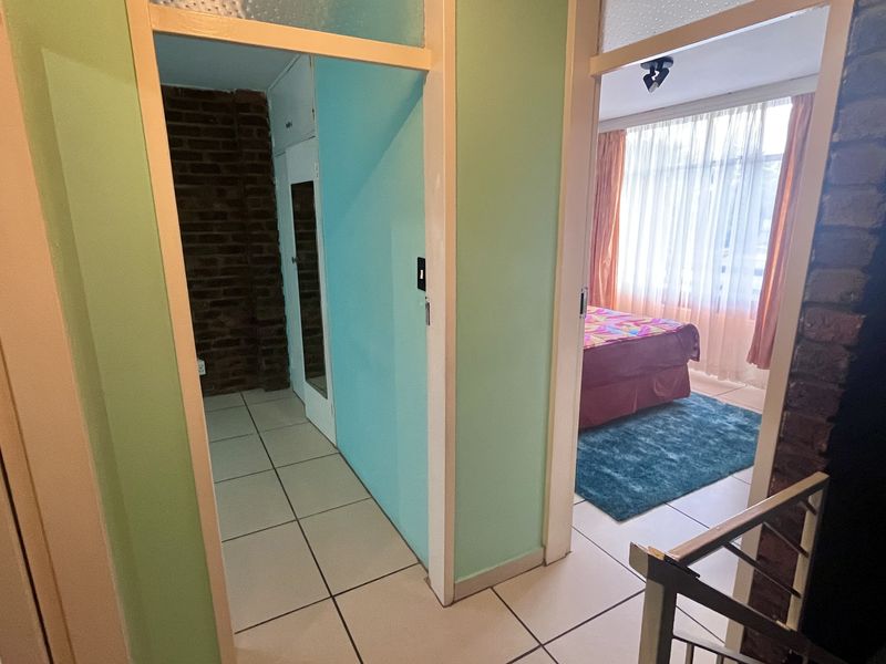 A hallway area featuring tiled flooring and an exposed brick wall, providing access to adjacent rooms including a bedroom.